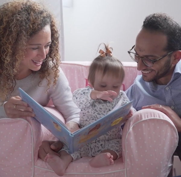 young adoptive mother and father read a book with toddler girl
