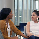 professional Black woman comforts Hispanic woman in a seated circle